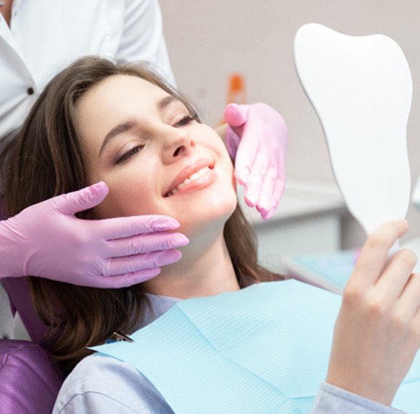 Woman using a mirror while visiting a dentist in Williamstown