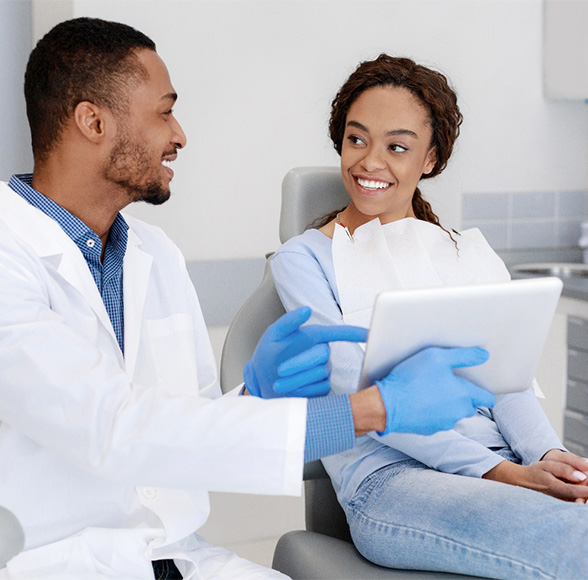 Dentist pointing to paper and discussing teeth whitening options with patient seated in examination chair.