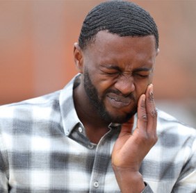 Man in patterned shirt rubbing jaw due to tooth pain