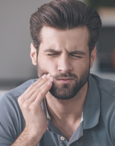 Man in need of emergency dentistry holding cheek in pain