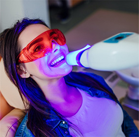 Woman with goggles in dental chair getting a professional in-office teeth whitening treatment.