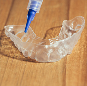 Closeup of a professional take-home teeth whitening kit on a wooden countertop.