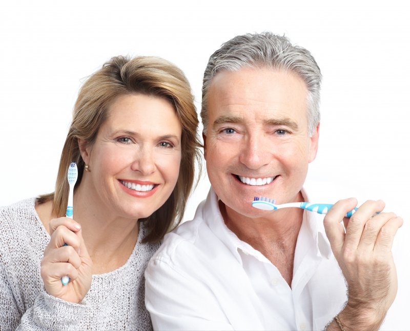 An older couple smiling and holding toothbrushes.