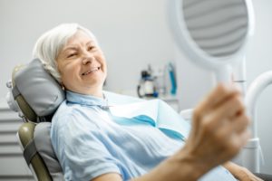 gray-haired woman admiring her smile in the mirror 