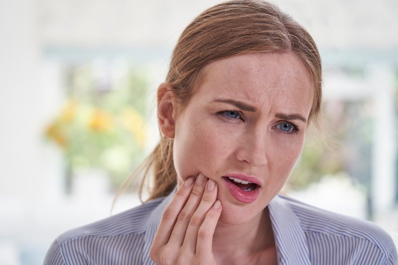 Young woman rubbing her jaw in concern