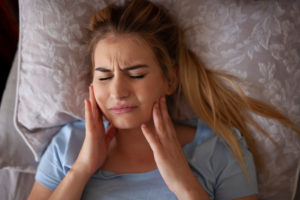Woman with bruxism holding her jaw in pain in bed
