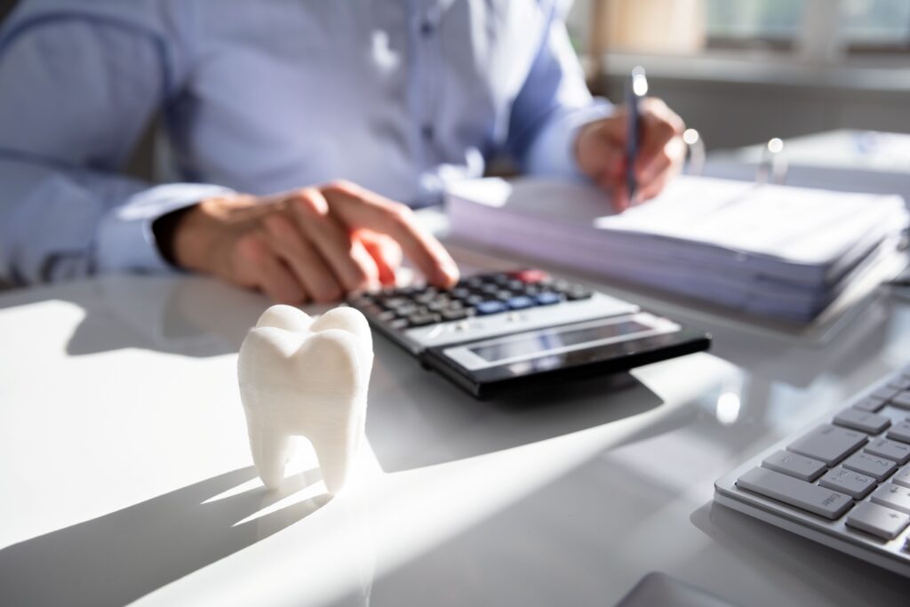 Someone at desk with calculator, invoices, and large model tooth