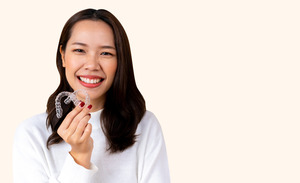 Woman in a white shirt holding two Invisalign aligners